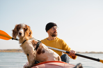 Man with a dog in a canoe on the lake. Young male person with spaniel in a kayak row boat, active...