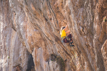 A strong woman climbs a beautiful orange rock.