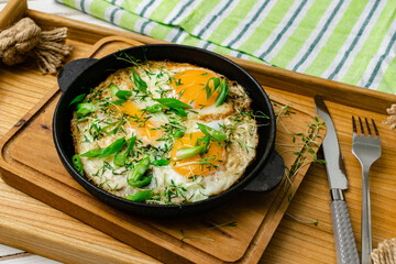 scrambled eggs with sprouts of greens and green onions in a frying pan on a wooden tray. Morning breakfast.