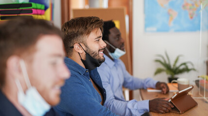 Young men at work in office meeting with video call while wearing protective face mask under chin - Business and alternative meeting