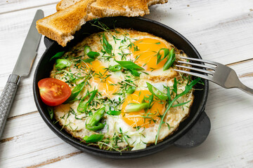 scrambled eggs with greens sprouts and green onions in a pan on a wooden background.