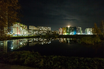 Fototapeta premium the new residential complex stands on the picturesque shore, sparkling with lights and reflected in the mirror-like surface of the lake