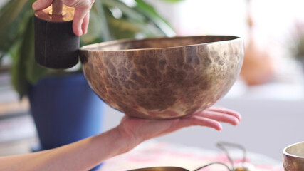 Woman playing on Tibetan singing bowl while sitting on yoga mat. Vintage tonned.