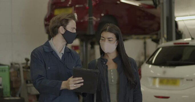 Car mechanic wearing face mask talking to customer during coronavirus pandemic in automotive workshop