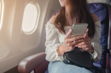 Young woman sitting near airplane window at sunset and using mobile phone during flight. Airplane,airport, travel concept.