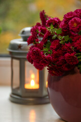 Autumn pink chrysanthemum flowers arranged in a violet vase with blurred lantern containing a candle on background