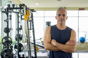 Fototapeta na wymiar Mature handsome Persian man with arms crossed at the gym