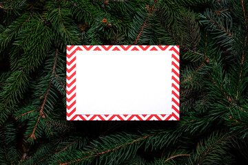 Christmas tree branches with paper card note. Nature New Year concept. Merry Christmas card, background. Congratulations, holidays, celebration. Mock up, copy space, flat lay. Red, green and white.