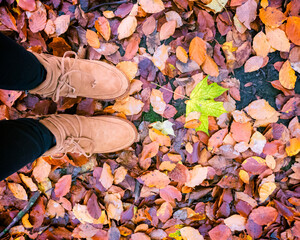 Young female with rubber winter shoes standing in a pile of fallen colorful autumn leaves