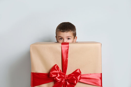 Cute little boy dressed as gift box near white wall. Christmas suit