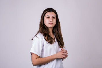 portrait of a nurse looking at the camera with interlocking fingers. Her uniform is white and her hair is long and brown.