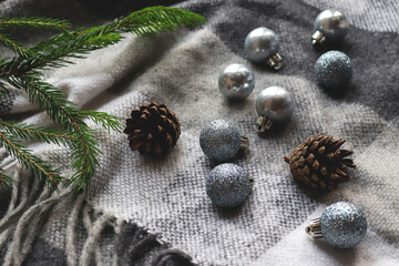 Festive Christmas background with selective focus. Christmas balls of silver color on a cozy gray blanket with pine cones and branch of a Christmas tree. Close-up, selective focus