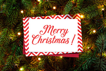 Christmas tree branches with paper wishing handwritten card. Nature New Year concept. Merry Christmas card, background. Congratulations, holidays, celebration. Red green and white. Ready to use, print