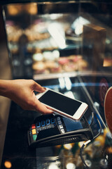 Woman paying in coffee shop using contactless method of payment via mobile phone. Woman using new way of payments