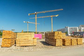 Piles of wood in front of large construction site with cranes