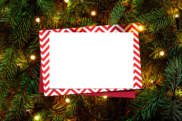 Christmas tree branches with paper card note and Christmas lights. Nature New Year concept. Merry Christmas card, background. Congratulations. Mock up, copy space, flat lay. Red, green and white.