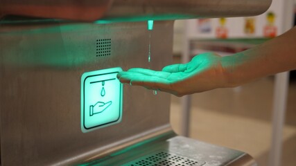 Side view of person using hands free sanitizer dispenser device in supermarket. Personal preventive...