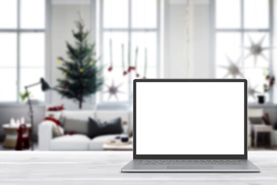 Blank display screen laptop computer on white wood table. Modern cozy comfortable home living room with Christmas decor. Home office desk workspace. Mock up copy space. Winter sales, online shopping