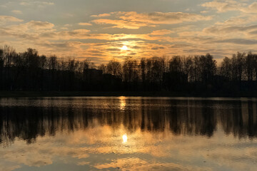 Leafless trees reflecting on rippled water surface of lake at sunset. Autumnal landscape