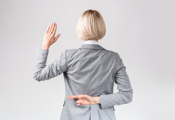 Female politician swearing oath with fingers crossed behind back on light grey studio background