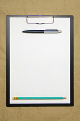 A tablet with a white sheet with pen and pencil on a beige craft paper. Concept of new opportunities, ideas, undertakings, innovations. Stock photo with empty place for your text and design.