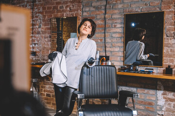 Young beautiful hairdresser woman with scissors in hand against a brick wall background. Barbershop advertising concept. Place for text or advertising