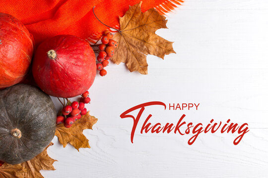Thanksgiving greetings. Pumpkins, dry leaves on a white background, top view. Kaligraphic capital inscription.