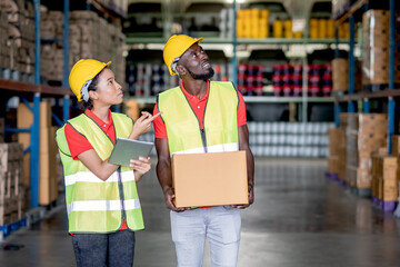 African American warehouse man and woman or factory worker work and discuss together about product box that man holding and walk together in workplace. Concept of good management of staff working.