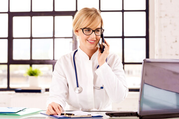 Smiling female doctor using phone and talking with her patient while sitting in doctor's office