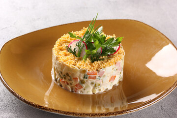 Russian cuisine. Olivier. Traditional salad with boiled vegetables, chicken fillet, sausage, egg, green peas and pickles on a beige plate. Restaurant menu. Background image, copy space