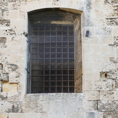 Fototapeta na wymiar Finestra antica con sbarre in ferro nelle mura medievali del castello Svevo a Bari. Sud Europa
