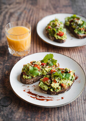 Two avocado toasts on white plate and glass of orange juice