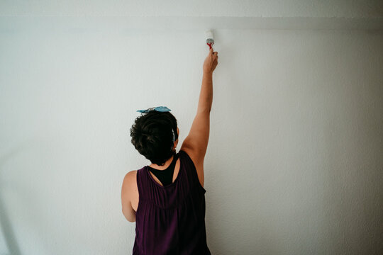 .Young woman dipping the roller in white paint to paint the walls of her room. Do it yourself. Lifestyle