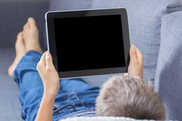 Teenage boy using digital tablet computer and showing blank screen lying on couch at home