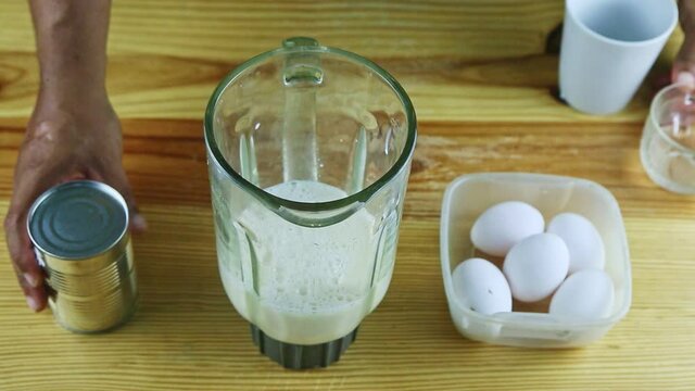 top view on man by hands pours canned milk into blender chalice with daily milk