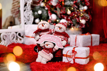 Snowmans with christmas gift boxes and new year tree and light bokeh on background. Translation: "Happy New year!"