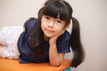 Portrait of cute Asian girl with black long hair lying on the bench, playing at playground, kid having fun and playing with friend