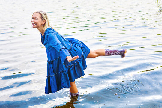 blond woman in blue dress standing in water with rubber boots