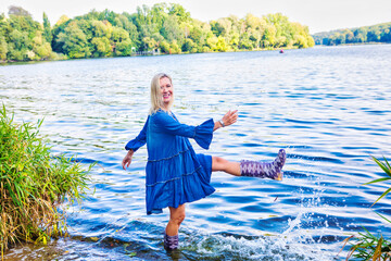 blond woman in blue dress standing in water with rubber boots