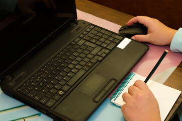 A person working on a laptop and writing in a Notepad