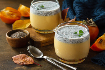 Autumn dessert. Homemade panna cotta with persimmon fruit and chia seeds on a wooden table.