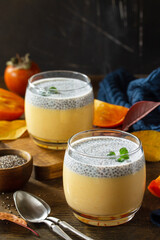Autumn dessert. Homemade panna cotta with persimmon fruit and chia seeds on a wooden table. Copy...