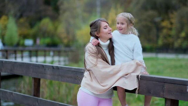 Cute little girl child kiss young mother in park show love and care, small preschooler daughter cuddle hug happy mom. oncept of warm family relationships and outdoor activities