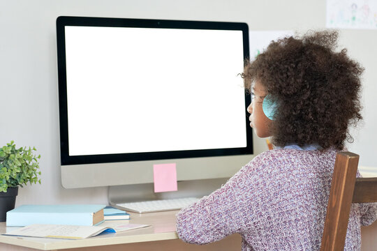 African american elementary school kid girl wearing headphones virtual distance learning online looking at mock up white blank computer screen remote digital elearning at home. Over shoulder view