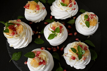 Obraz na płótnie Canvas dessert called Anna Pavlova. Meringue with cream garnished with pomegranate, tangerine slices and Basil leaves