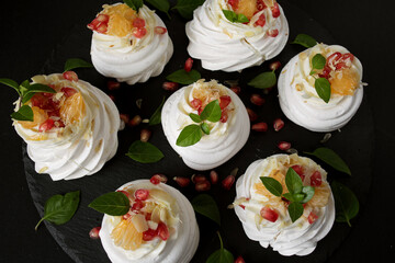 dessert called Anna Pavlova. Meringue with cream garnished with pomegranate, tangerine slices and Basil leaves