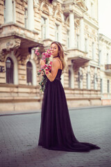 
girl in a black dress and a bouquet of flowers on the street of the old city