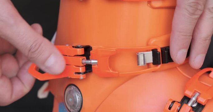 Adjusting boot buckle on orange ski boot - close up of male fingers tightening the boot by one increment, side view. Preparation for skiing, essential ski gear, winter sport.