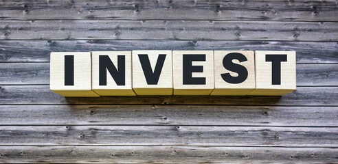invest word written on wooden block and on brown table
