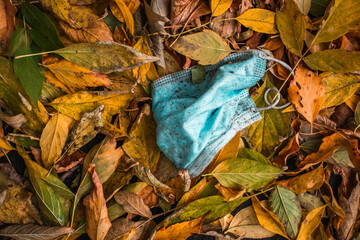 A mask and gloves were used for medical protection lost on the ground. Disposable mask lying on the street. Incorrectly discarding the used face mask, on plant leaves in autumn. High quality photo